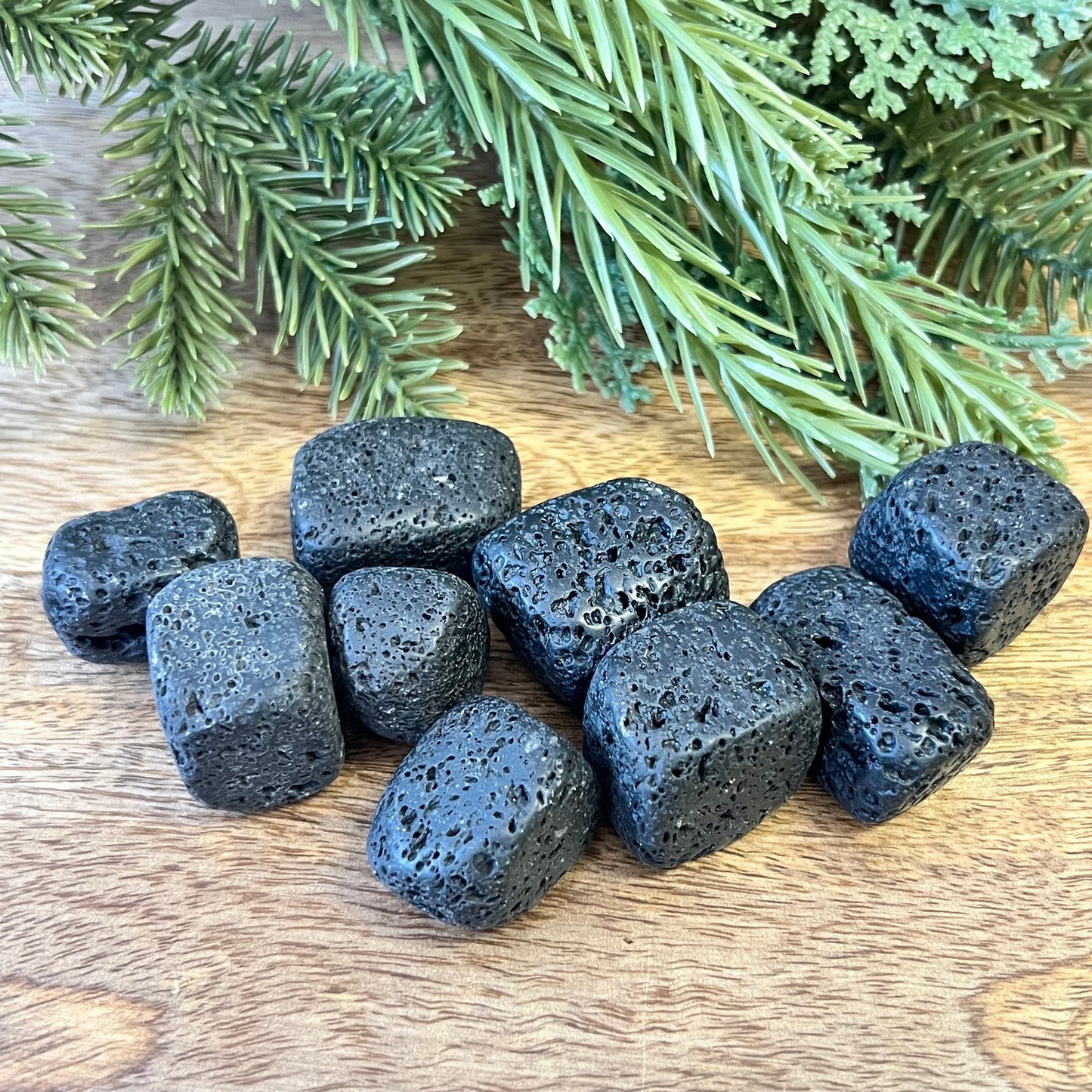 Group of semi-polished Lava Stone crystal tumbles on a wooden board. They are a satin matte texture with lots of natural holes