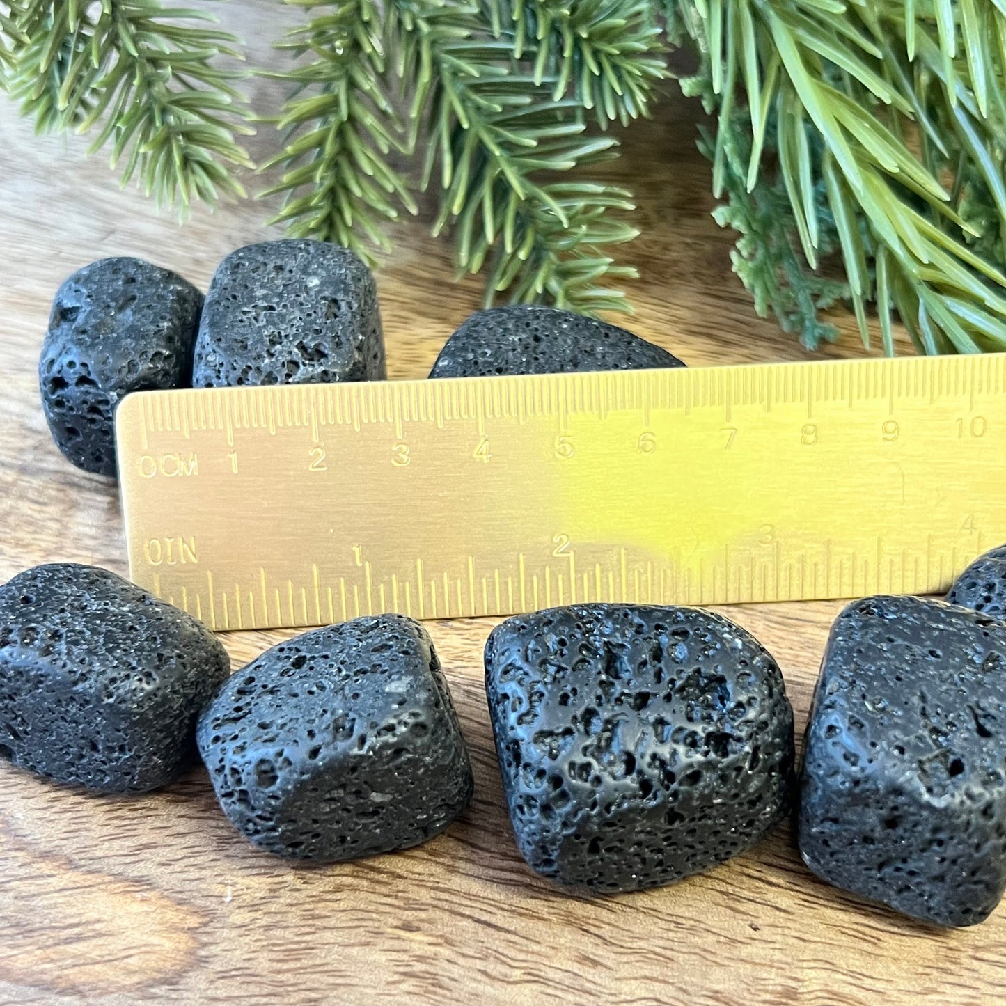 Group of semi-polished Lava Stone crystal tumbles next to a ruler. They are a satin matte texture with lots of natural holes