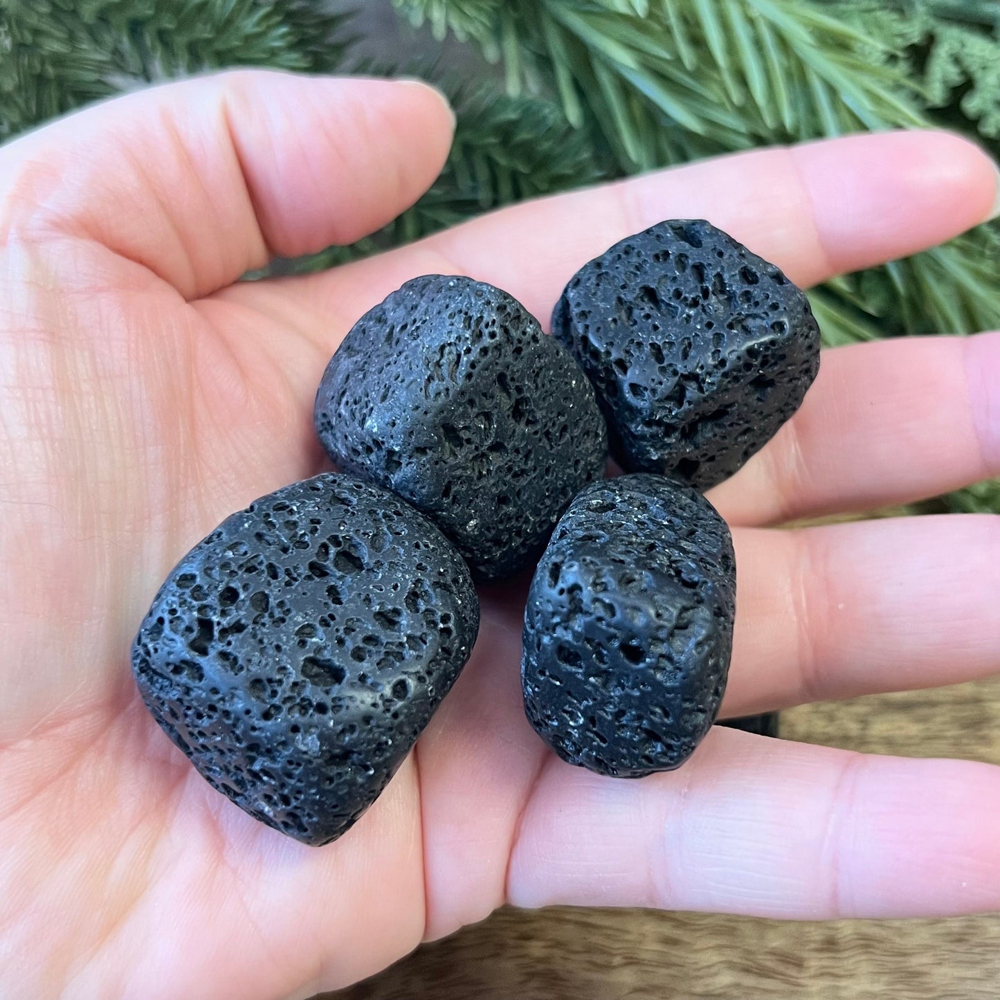 Group of semi-polished Lava Stone crystal tumbles in a person's hand. They are a satin matte texture with lots of natural holes