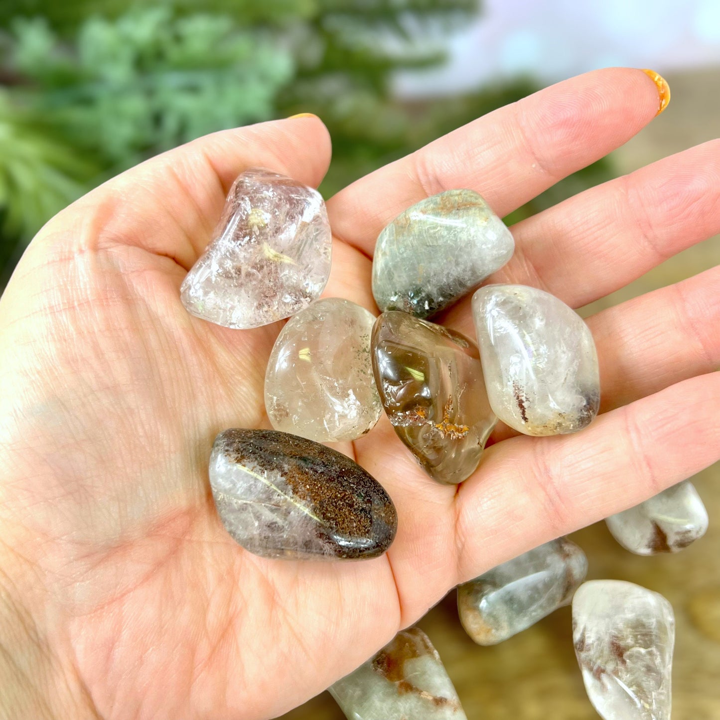 a person's hand holding a group of tumbled lodolite Garden Quartz crystals