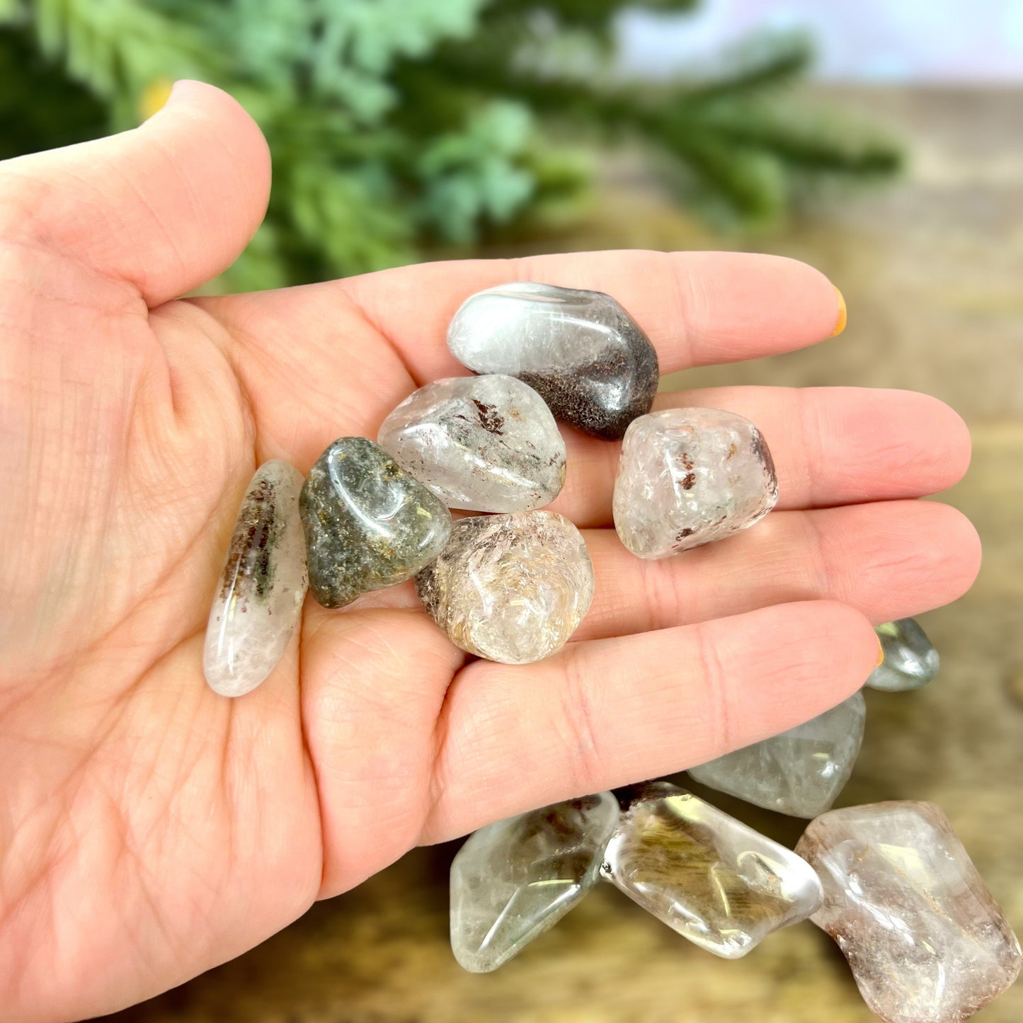 a person's hand holding a group of tumbled lodolite Garden Quartz crystals