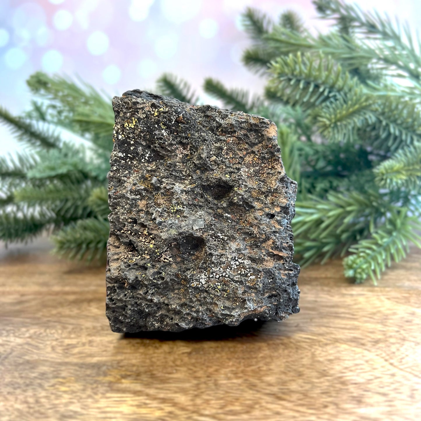 Image of a large, rough chunk of black Lava Rock Stone on a wooden table. Has rough texture with lots of holes.
