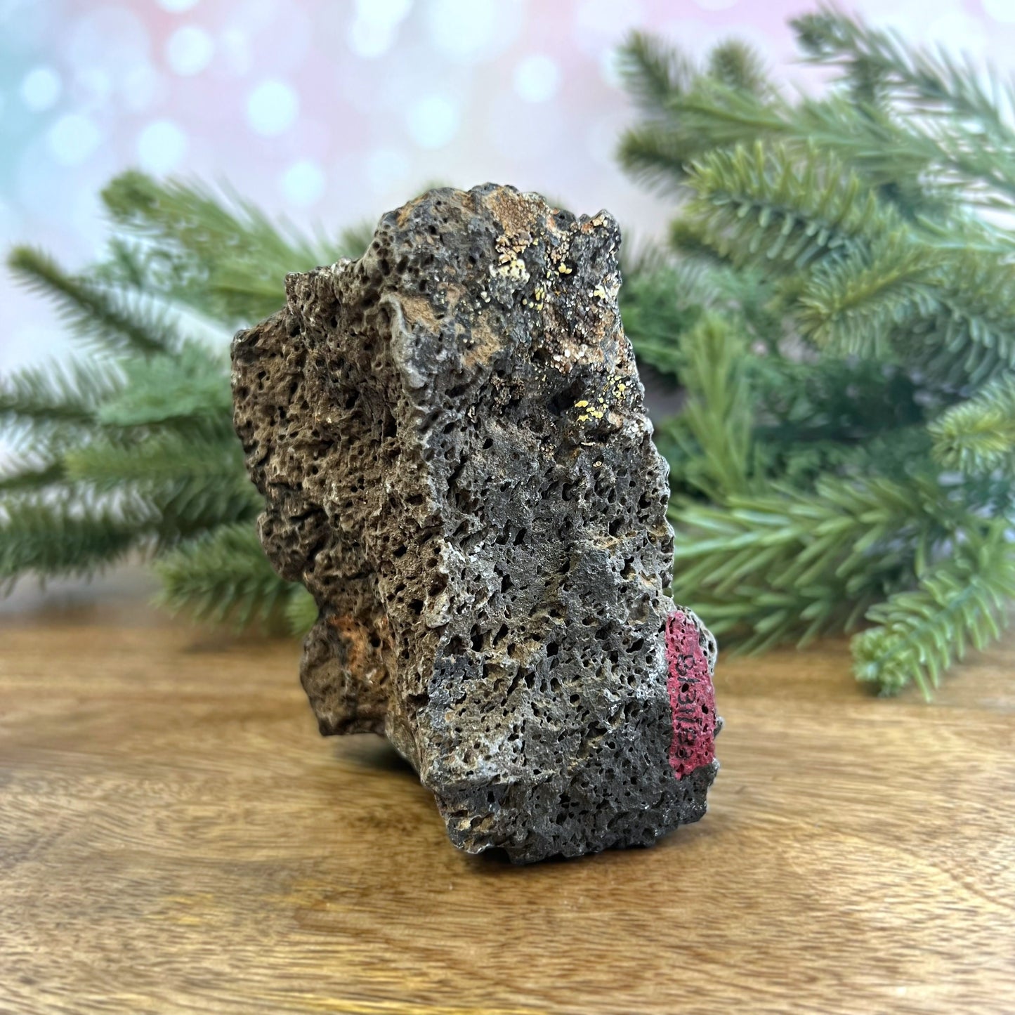 Image of a large, rough chunk of black Lava Rock Stone on a wooden table. Has rough texture with lots of holes.
