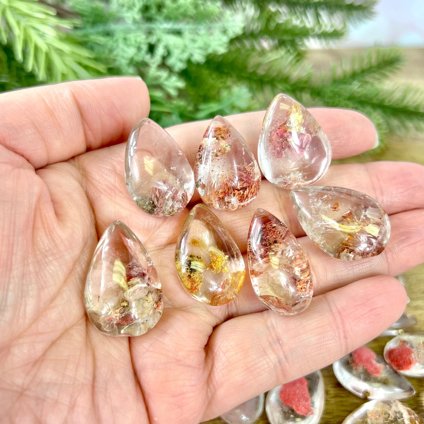 a group of dyed red Garden Quartz tumbled crystals in a teardrop shape, resting in a person's hand