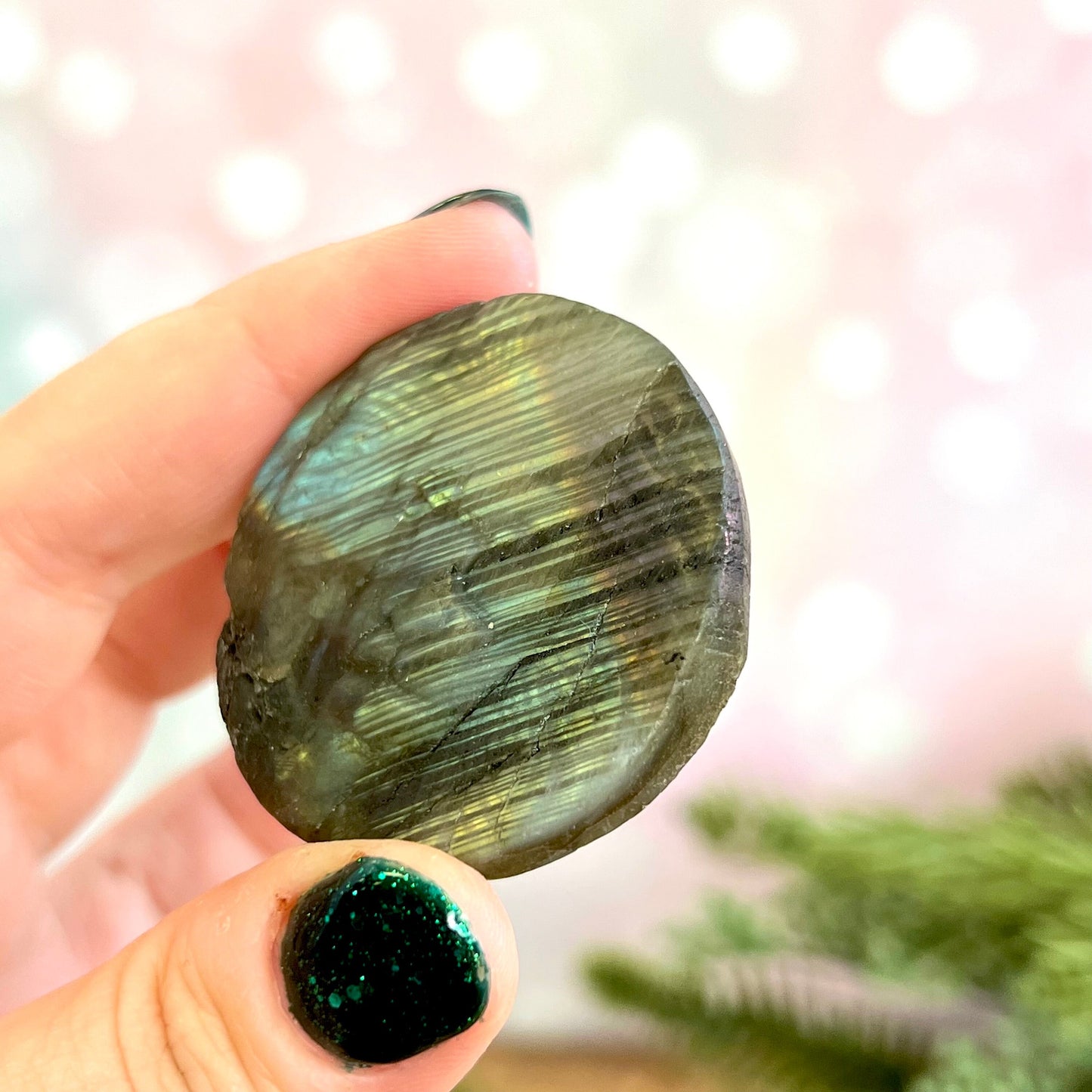 Image of a round carved stone cabochon made from Labradorite crystal. On the front is a lion's head, and the back is flat.