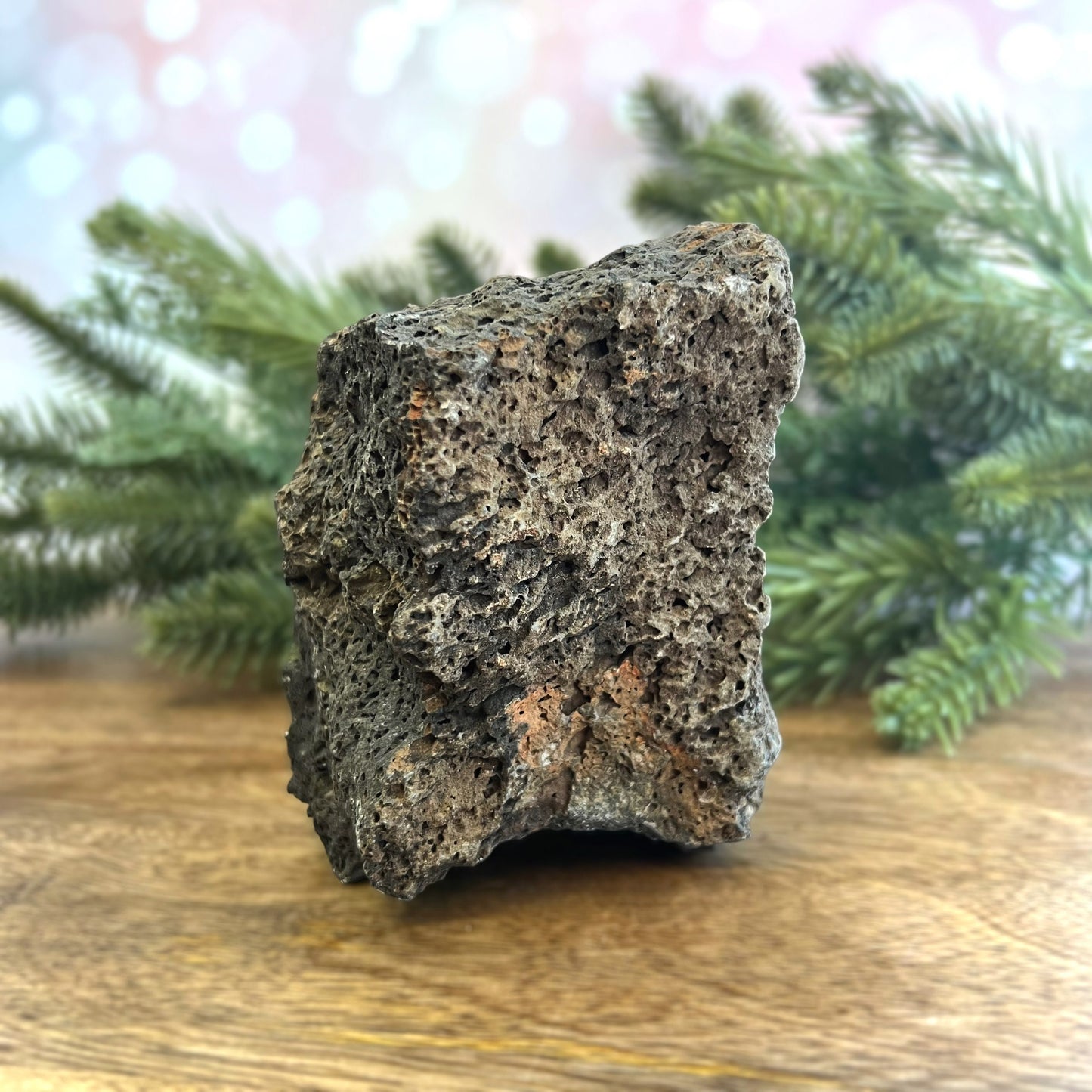 Image of a large, rough chunk of black Lava Rock Stone on a wooden table. Has rough texture with lots of holes.