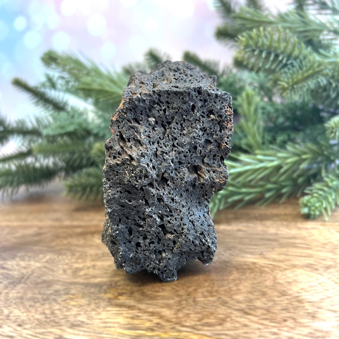 Image of a large, rough chunk of black Lava Rock Stone on a wooden table. Has rough texture with lots of holes.