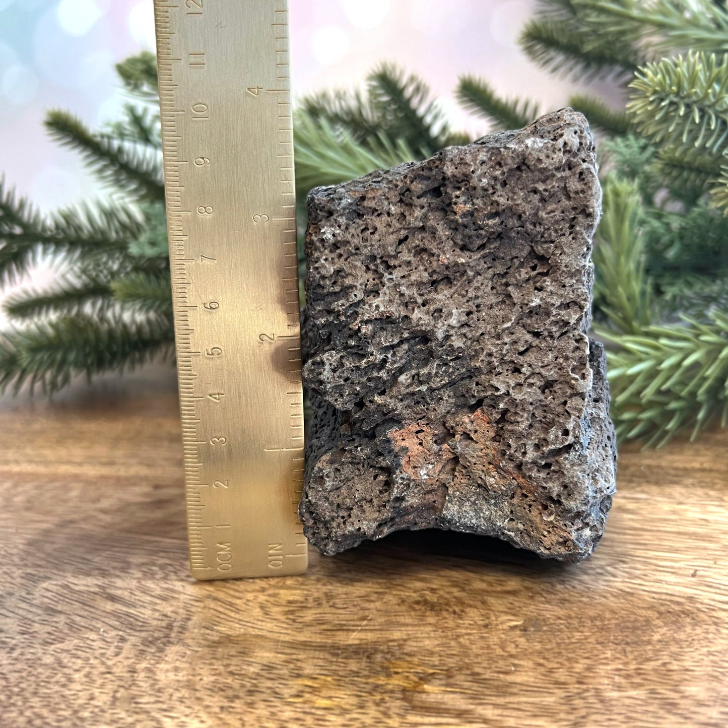 Image of a large, rough chunk of black Lava Rock Stone on a wooden table. Has rough texture with lots of holes.