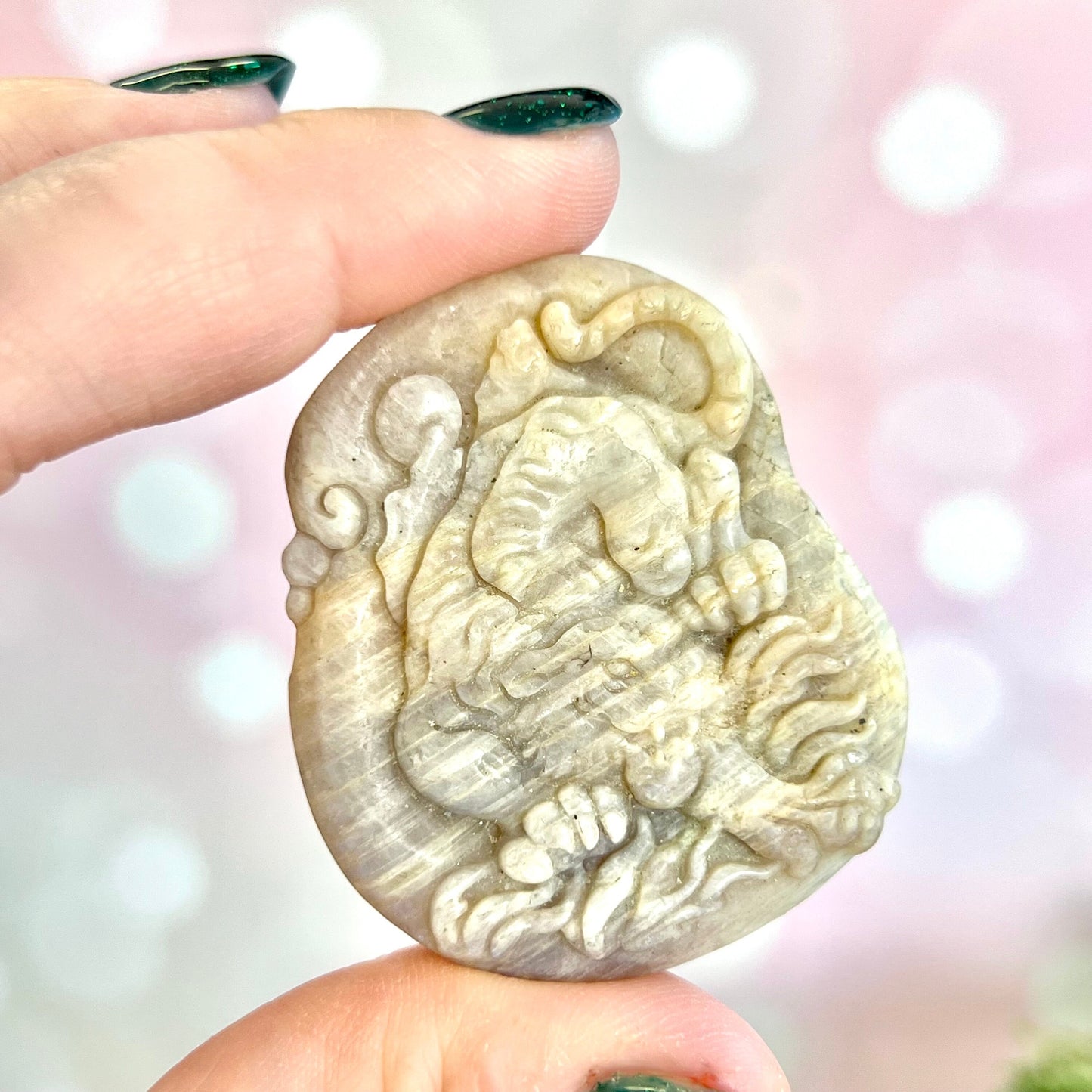 Image of a carved cabochon featuring a crouching tiger mid roar. The front is carved and the back is flat. It's made from Sunstone in Moonstone crystal.