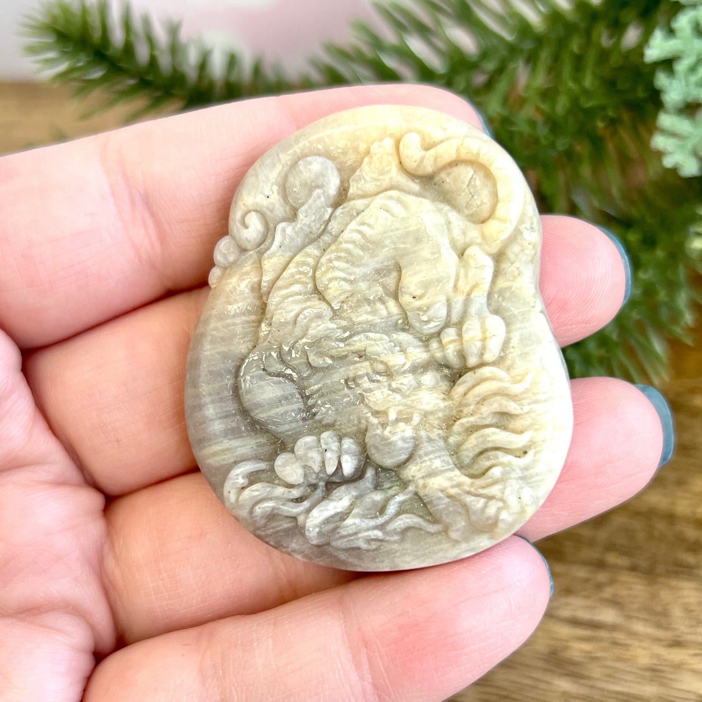 Image of a carved cabochon featuring a crouching tiger mid roar. The front is carved and the back is flat. It's made from Sunstone in Moonstone crystal.