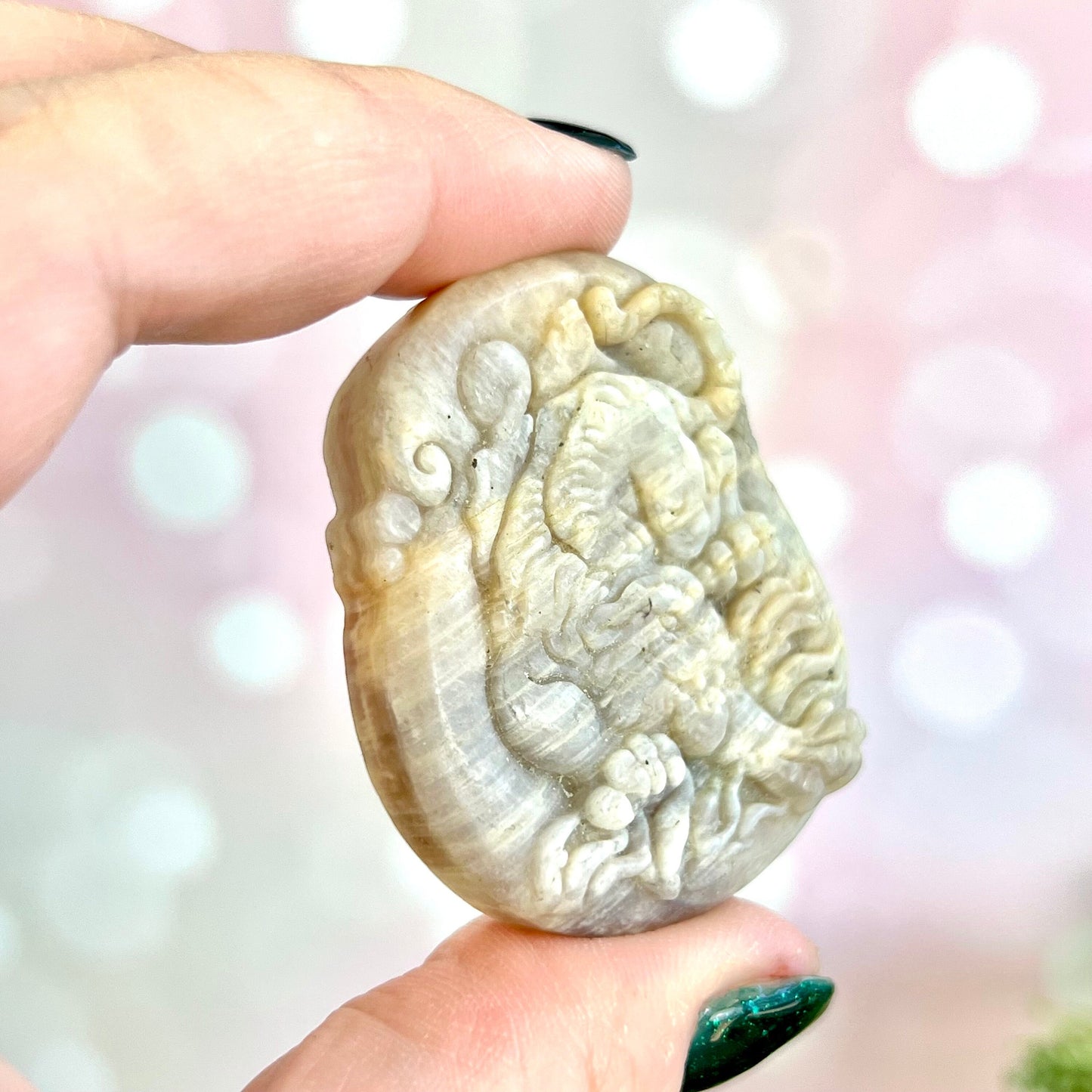 Image of a carved cabochon featuring a crouching tiger mid roar. The front is carved and the back is flat. It's made from Sunstone in Moonstone crystal.