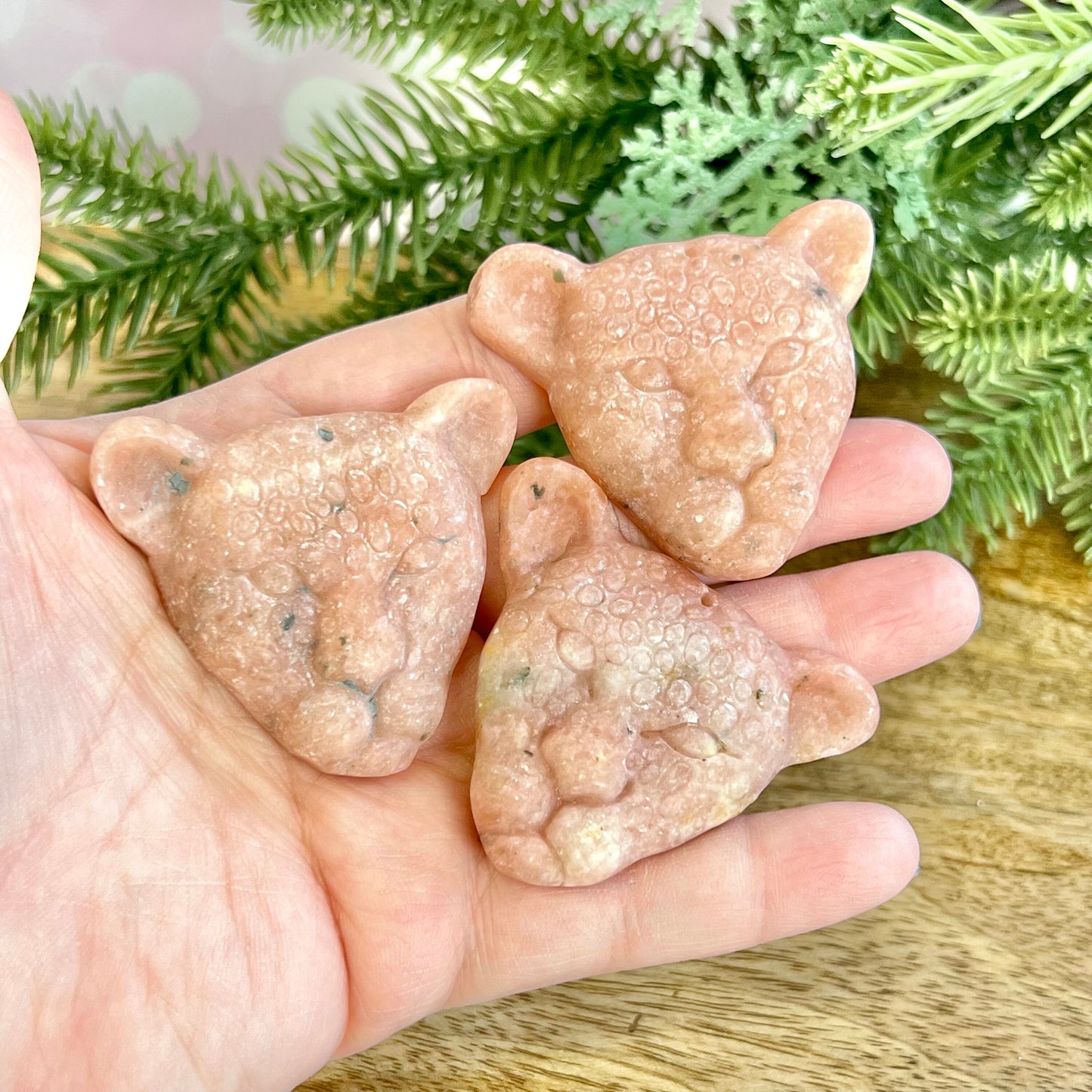 Group of three Orange Calcite carved stone cabochons in the shape of leopard heads in a person's hand