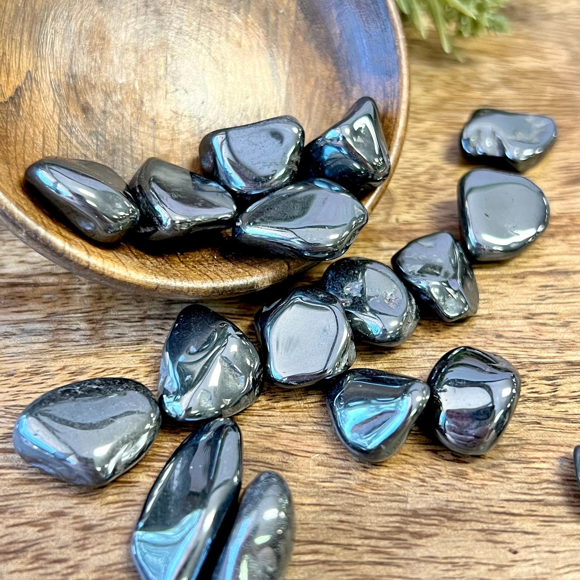 Group of polished Hematite crystal tumbles in a wooden bowl. They are a metallic looking black color and smooth.