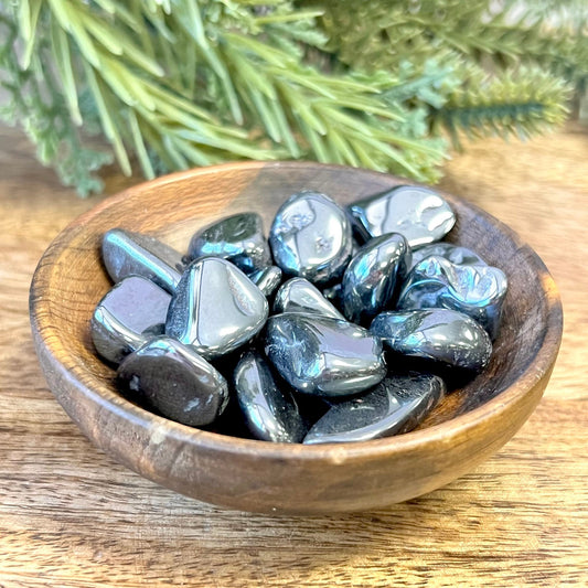 Group of polished Hematite crystal tumbles in a wooden bowl. They are a metallic looking black color and smooth.