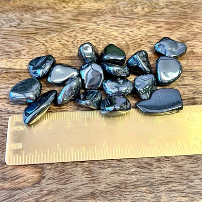 Group of polished Hematite crystal tumbles next to a ruler. They are a metallic looking black color and smooth.