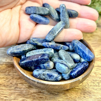 a group of blue and white sodalite tumbled crystals in a wooden bowl. They are long oval dagger shapes