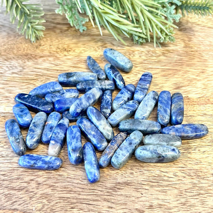 a group of blue and white sodalite tumbled crystals on a wooden background. They are long oval dagger shapes