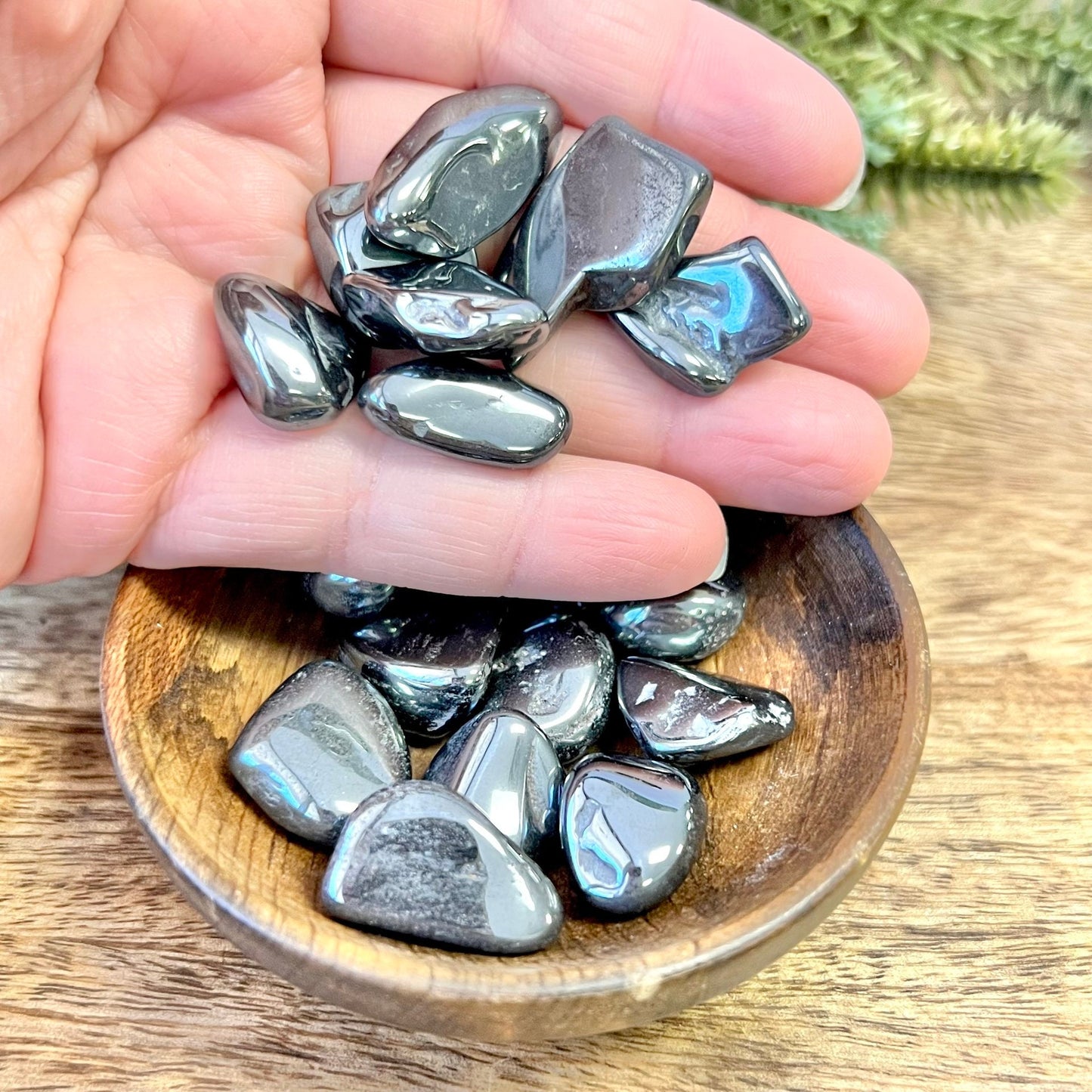 Group of polished Hematite crystal tumbles in a person&#39;s hand. They are a metallic looking black color and smooth.