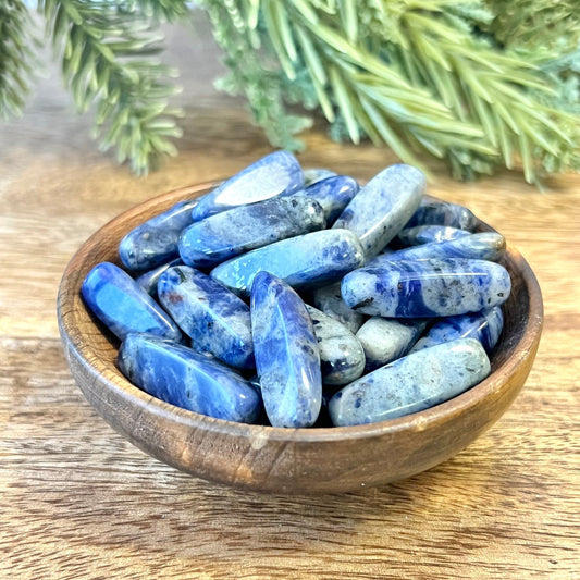 a group of blue and white sodalite tumbled crystals in a wooden bowl. They are long oval dagger shapes