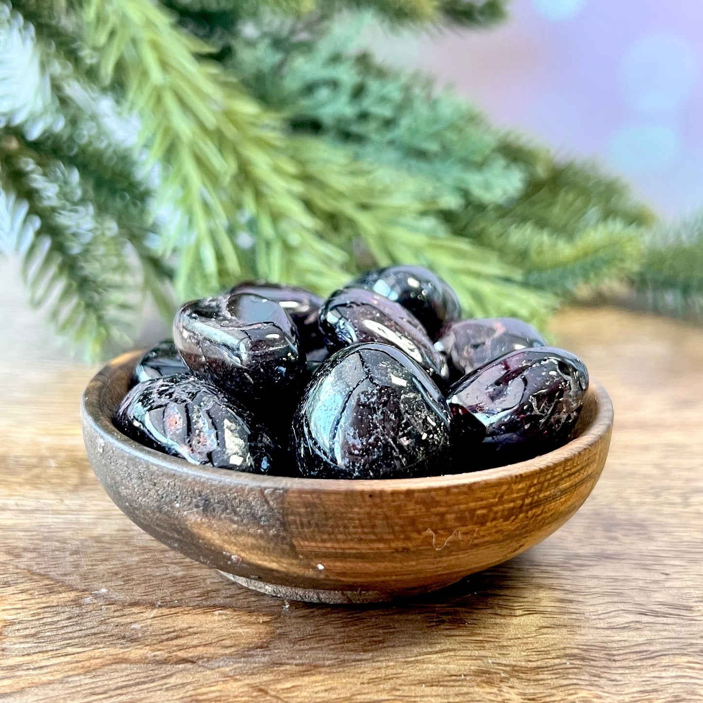 a group of very dark red garnet tumbled crystals in a wooden bowl