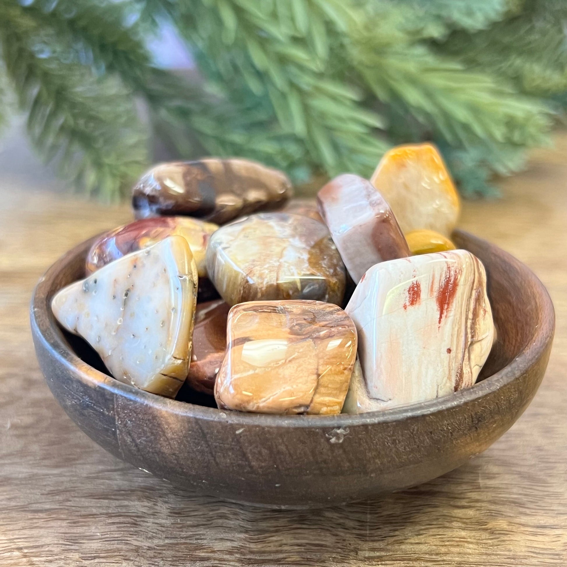 a group of colorful petrified Wood tumbled crystals in a wooden bowl