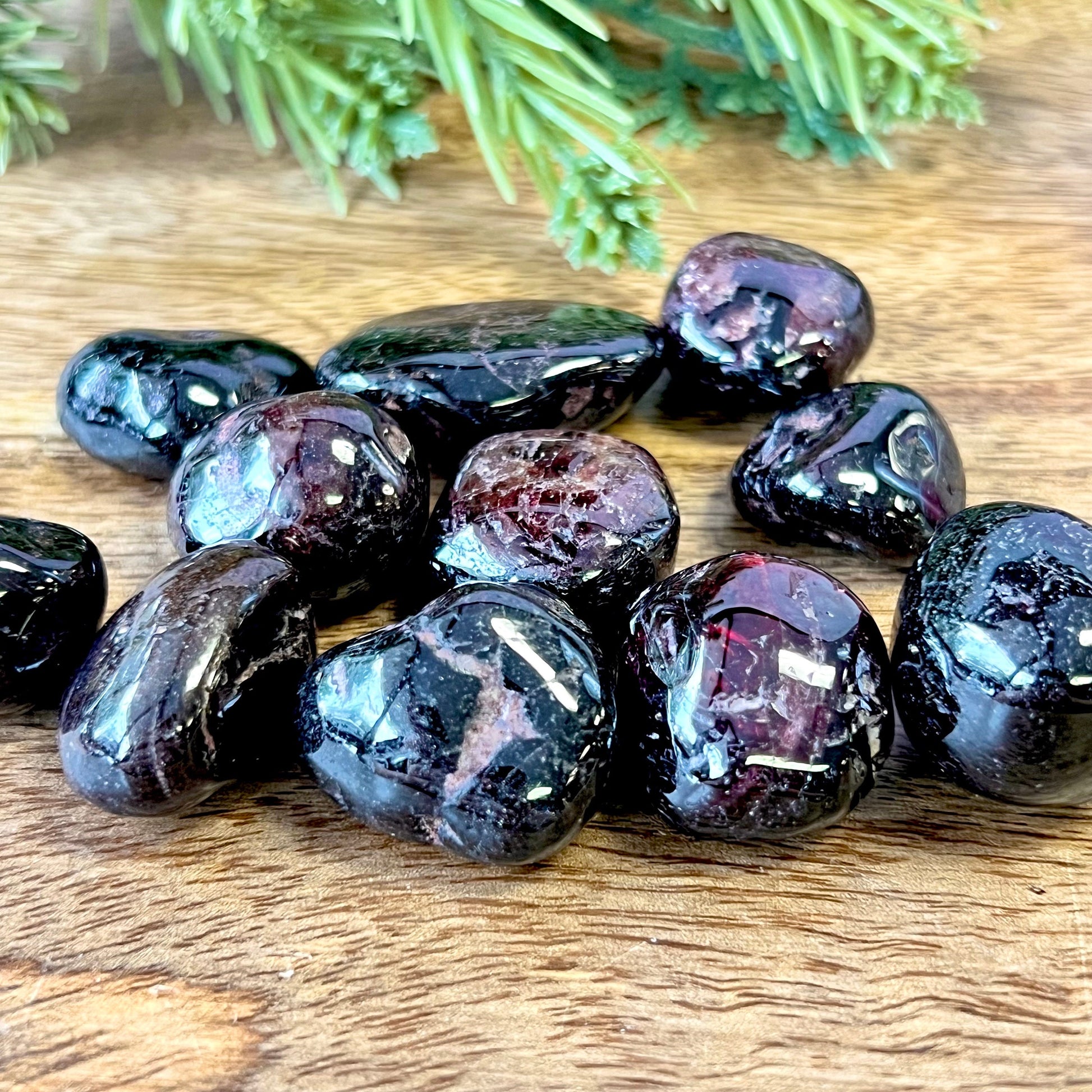 a group of very dark red garnet tumbled crystals on a wooden surface