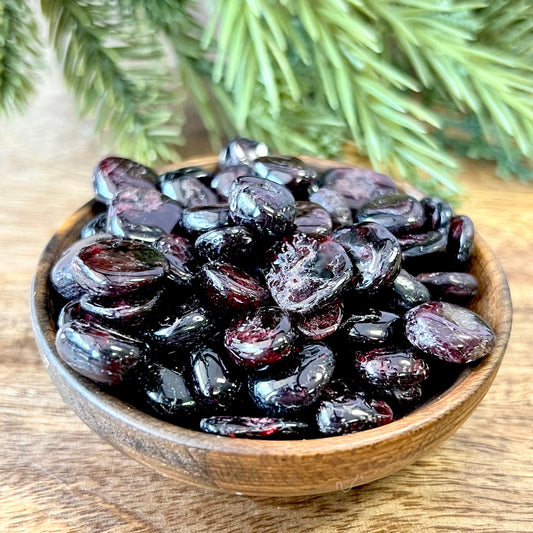 Group of small miniature tumbled crystals in a wooden bowl. They are a dark red garnet, and similar to crystal chips.