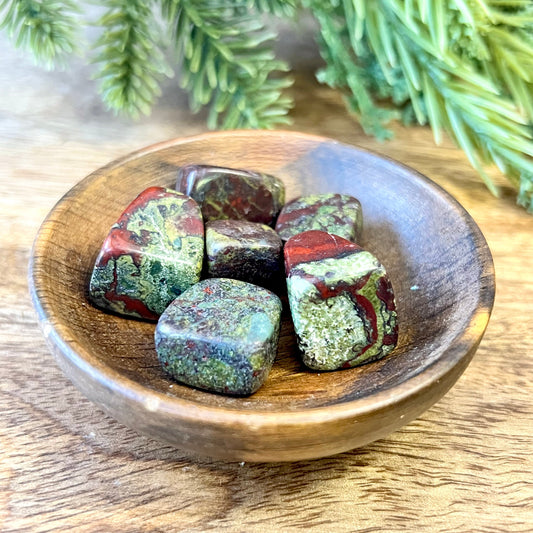 Group of green and red tumbled crystals in a wooden bowl. They are Dragon Blood Stone, and a polished cube shape.