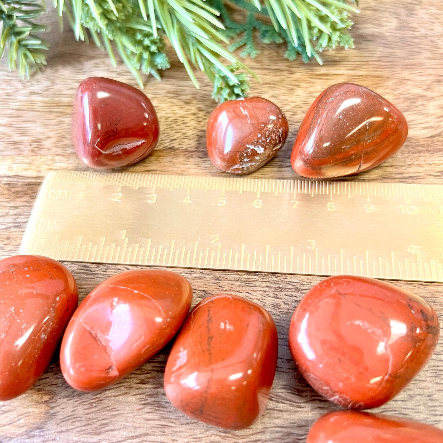a group of large red Jasper tumbled crystals next to a gold ruler