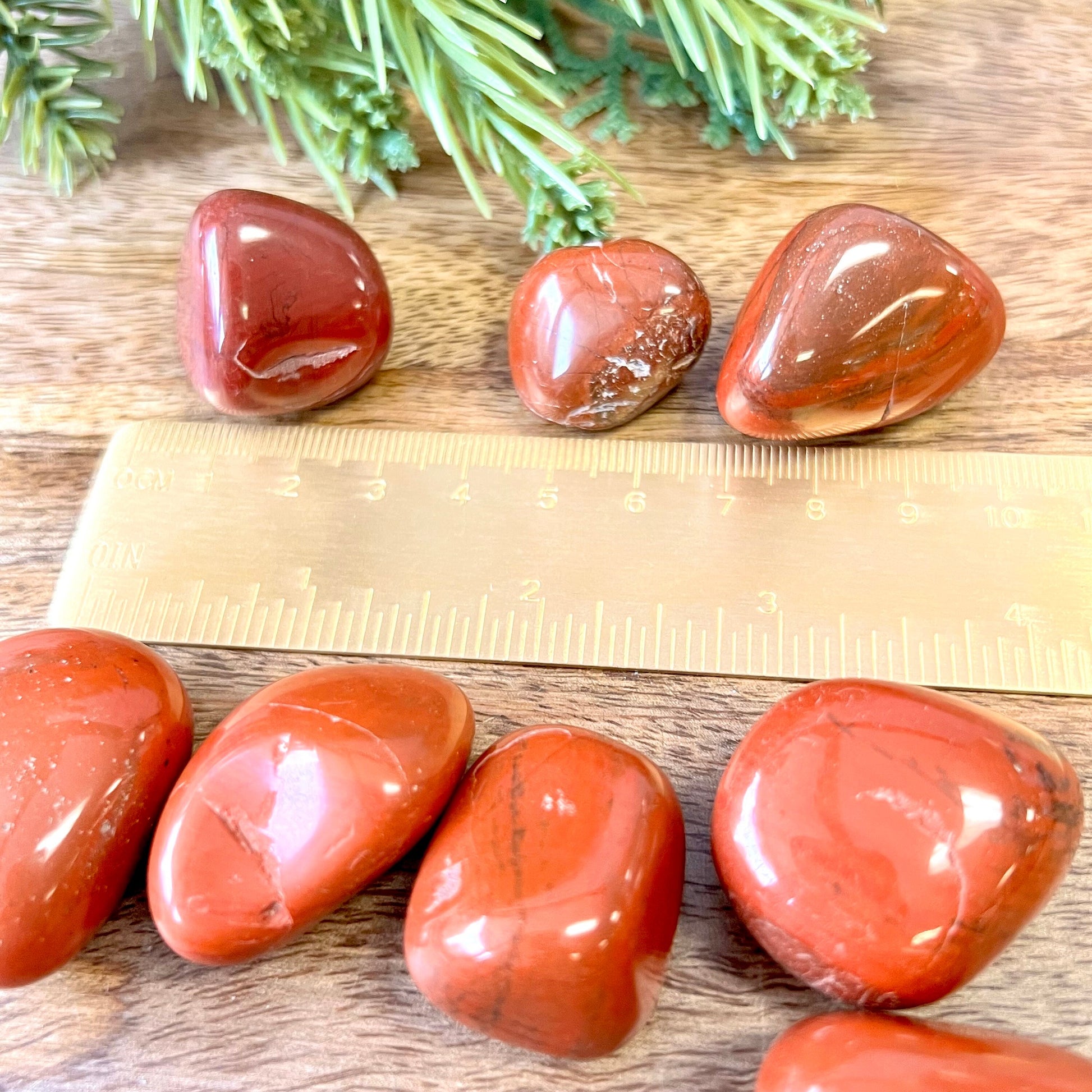 a group of large red Jasper tumbled crystals next to a gold ruler