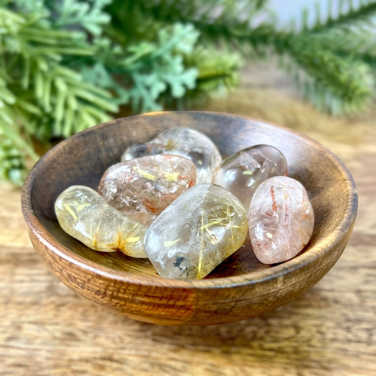 a group of Golden rutilated quartz tumbled crystals in a wooden bowl