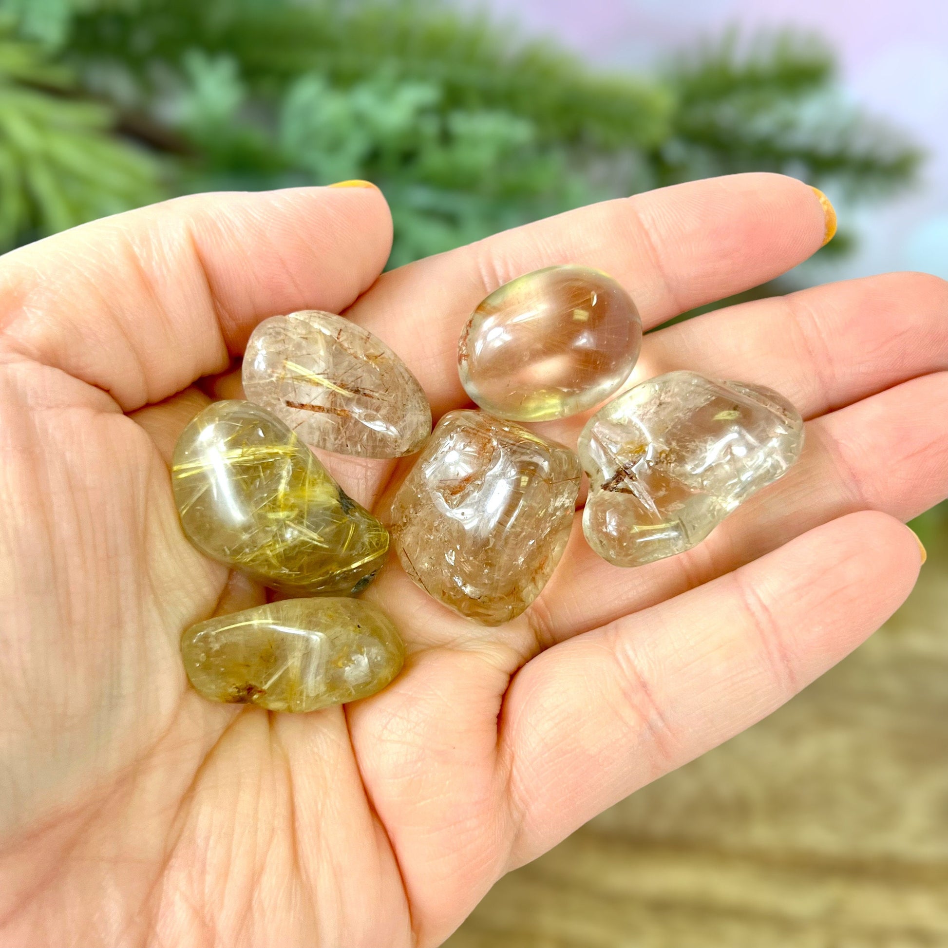 a person&#39;s hand holding a group of Golden rutilated quartz tumbled crystals