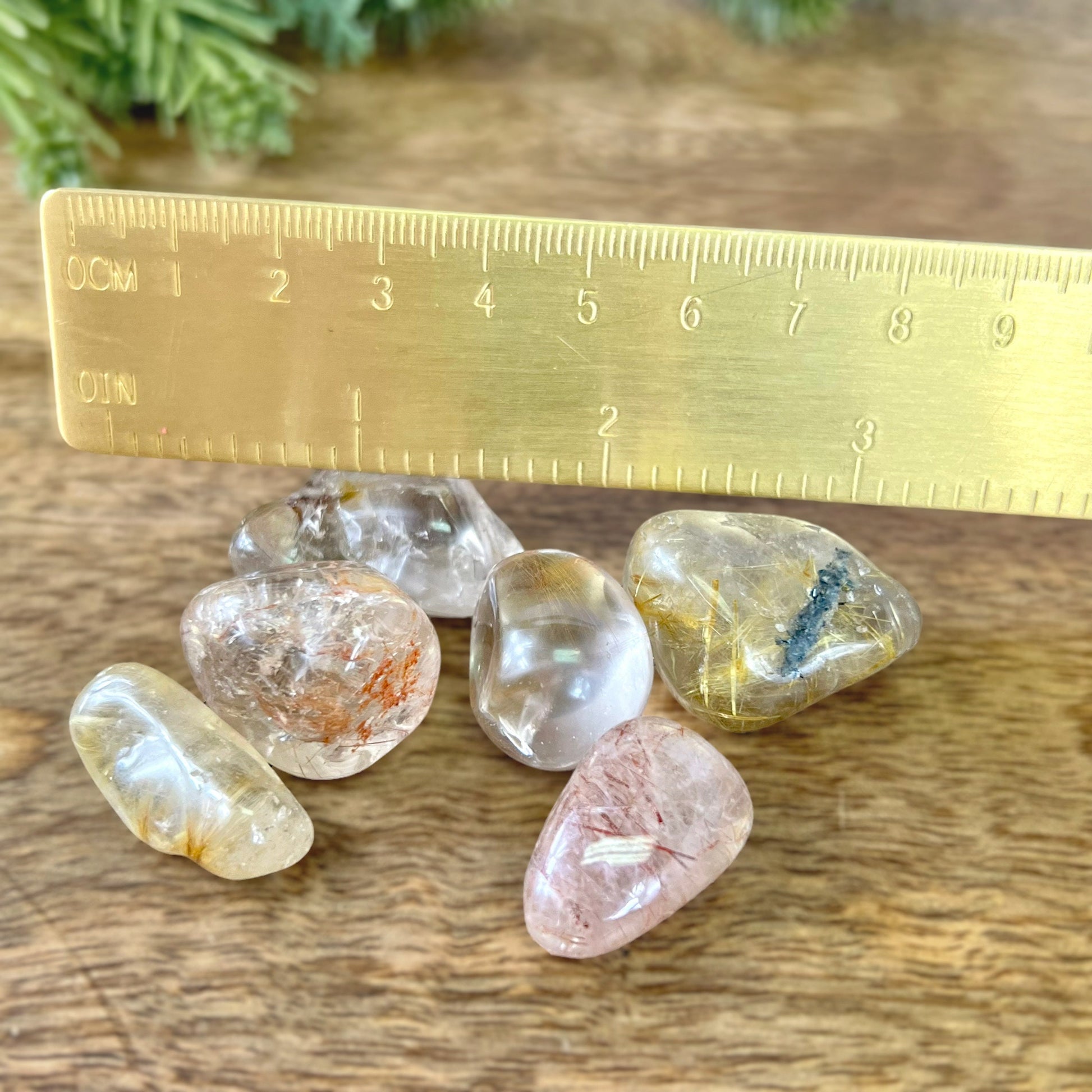 a group of Golden rutilated quartz tumbled crystals next to a gold ruler