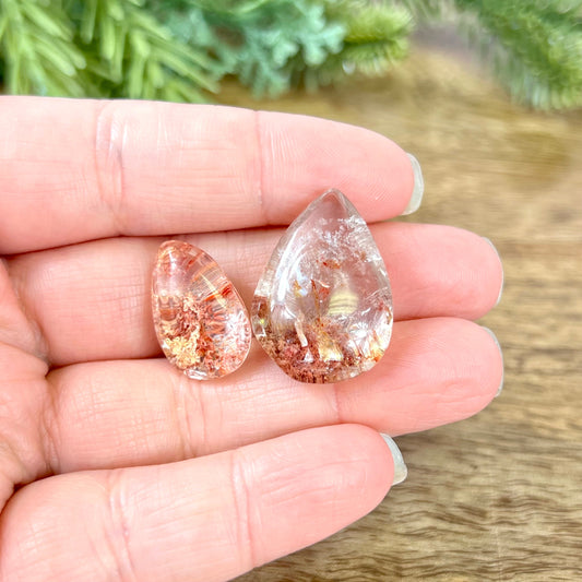 a group of dyed red Garden Quartz tumbled crystals in a teardrop shape, resting in a person&#39;s hand