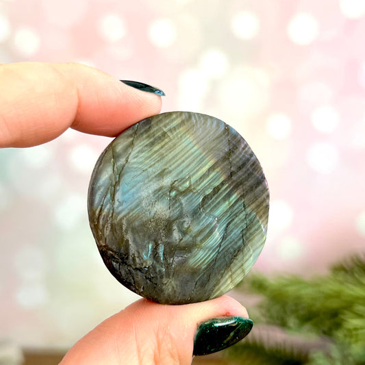 Image of a round carved stone cabochon made from Labradorite crystal. On the front is a lion&#39;s head, and the back is flat.