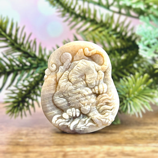 Image of a carved cabochon featuring a crouching tiger mid roar. The front is carved and the back is flat. It&#39;s made from Sunstone in Moonstone crystal.